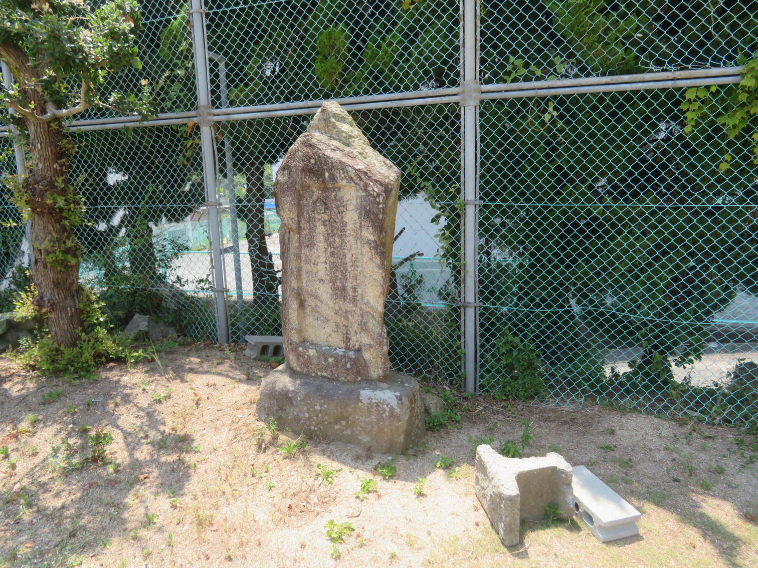 フェンス脇に立つ銘文の風化した石碑