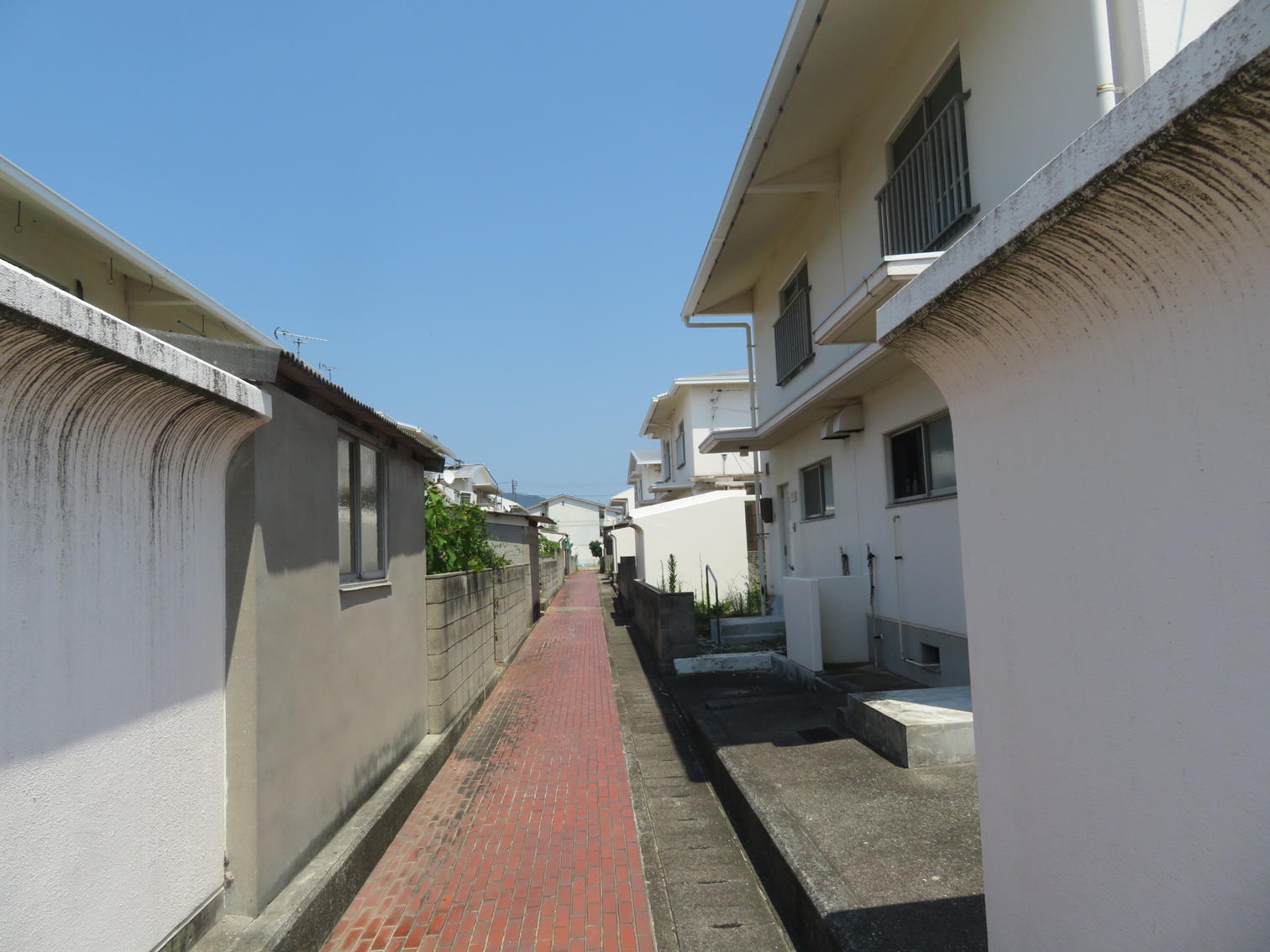 白い住宅の間の赤いれんが敷きの路地