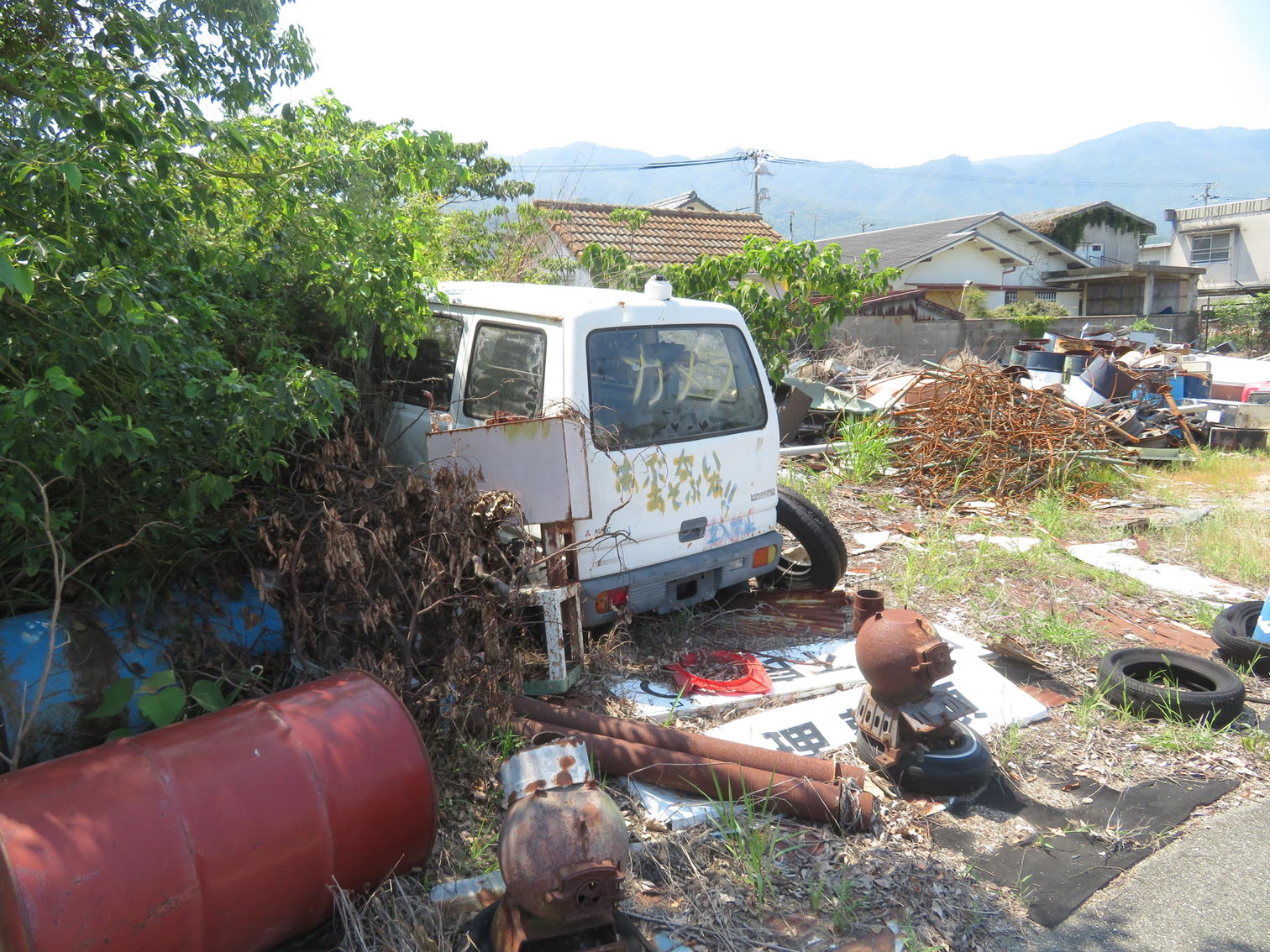 草に埋もれた廃車とドラム缶や廃材