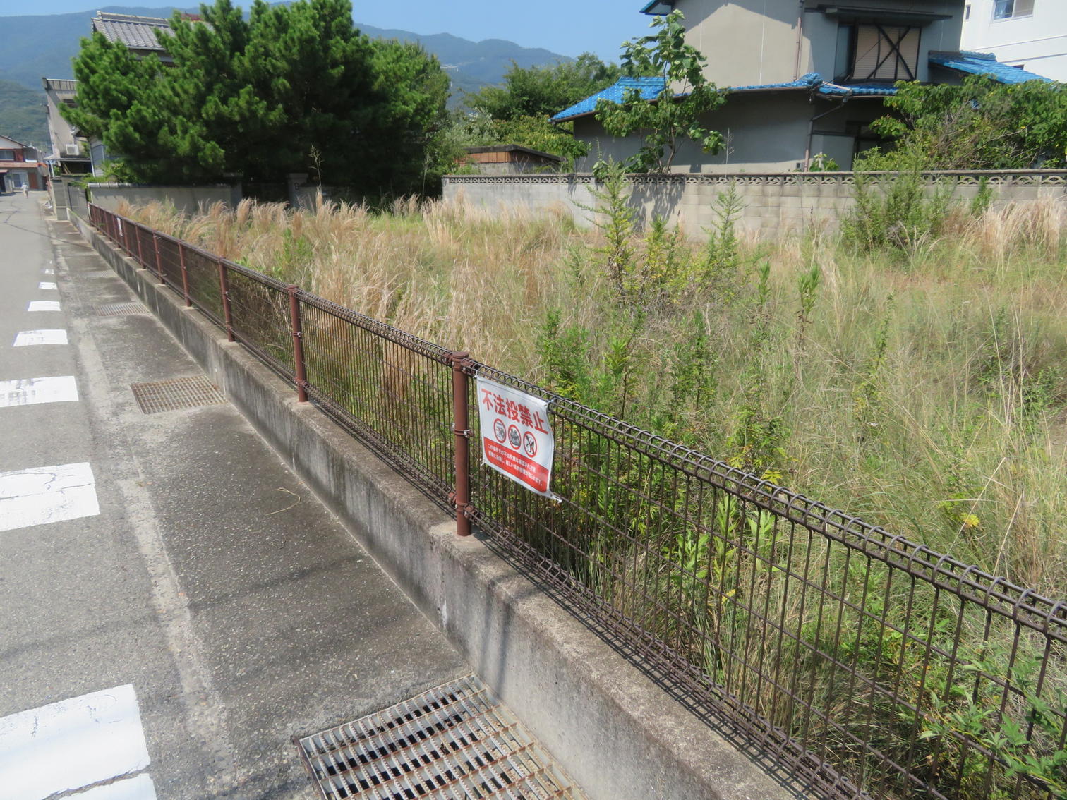 不法投棄禁止の札が付いた柵と草の茂る空き地