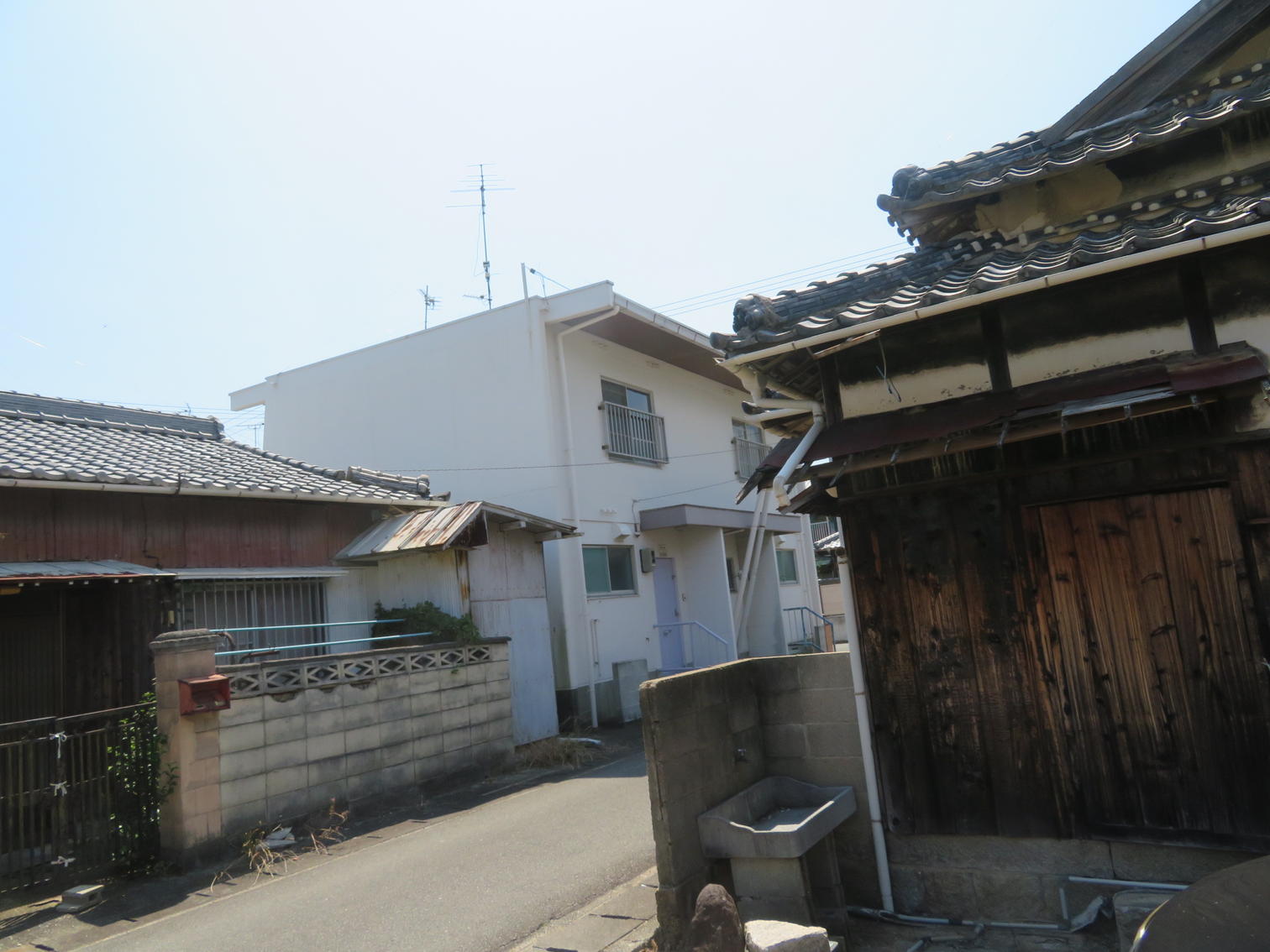 木造の蔵と白い改良住宅が向かい合う路地