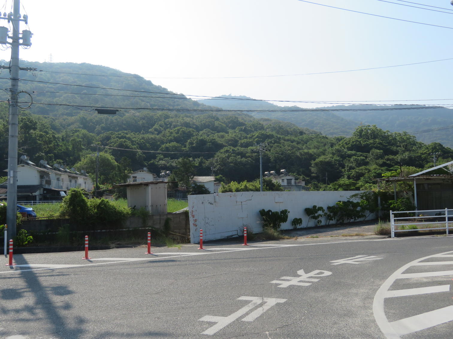 港からの道が交わる角。白い塀の向こうに家並みと山が見える。