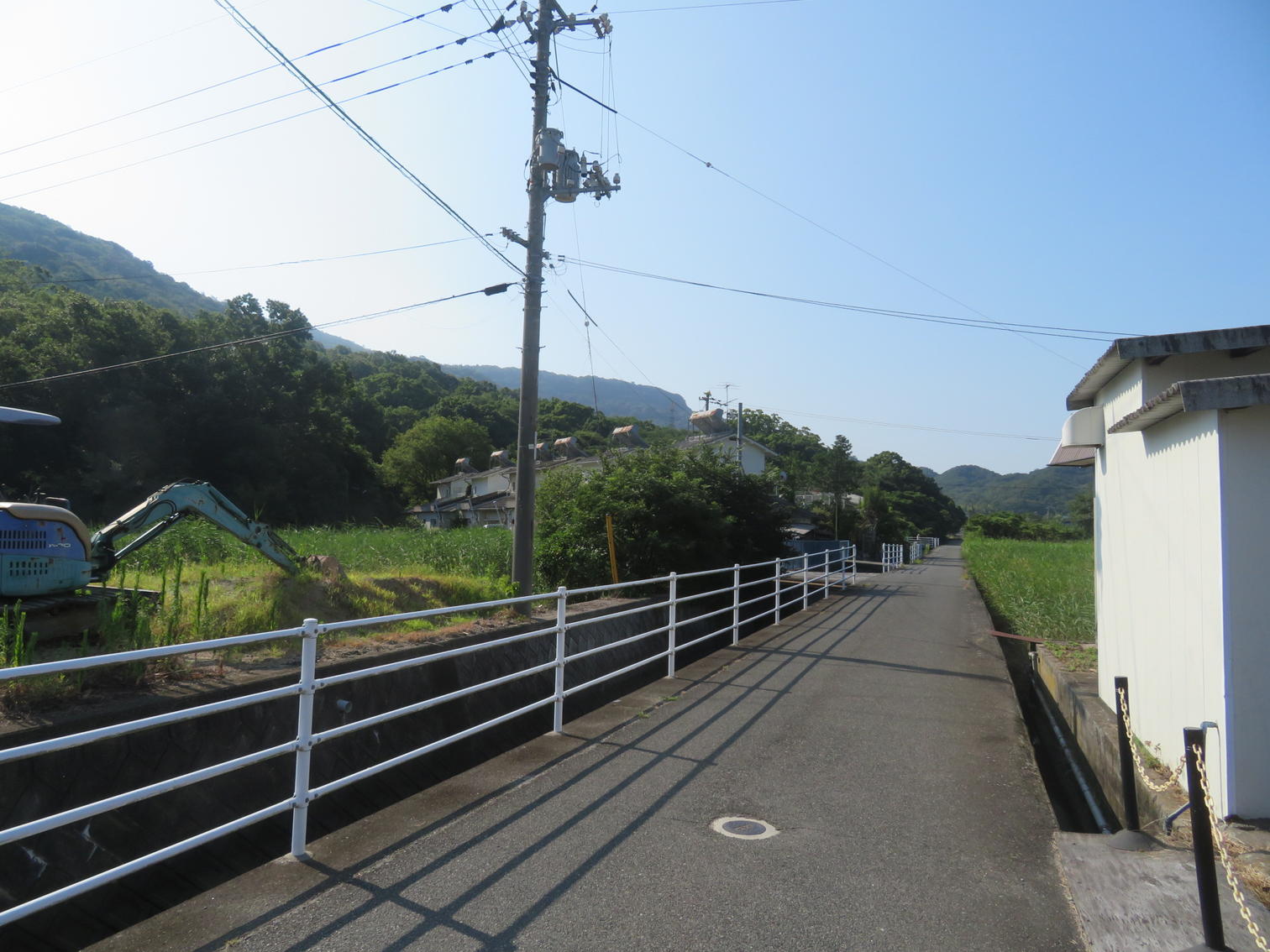 水路に沿って白い手すりの道が延びる。奥に重機が見える。