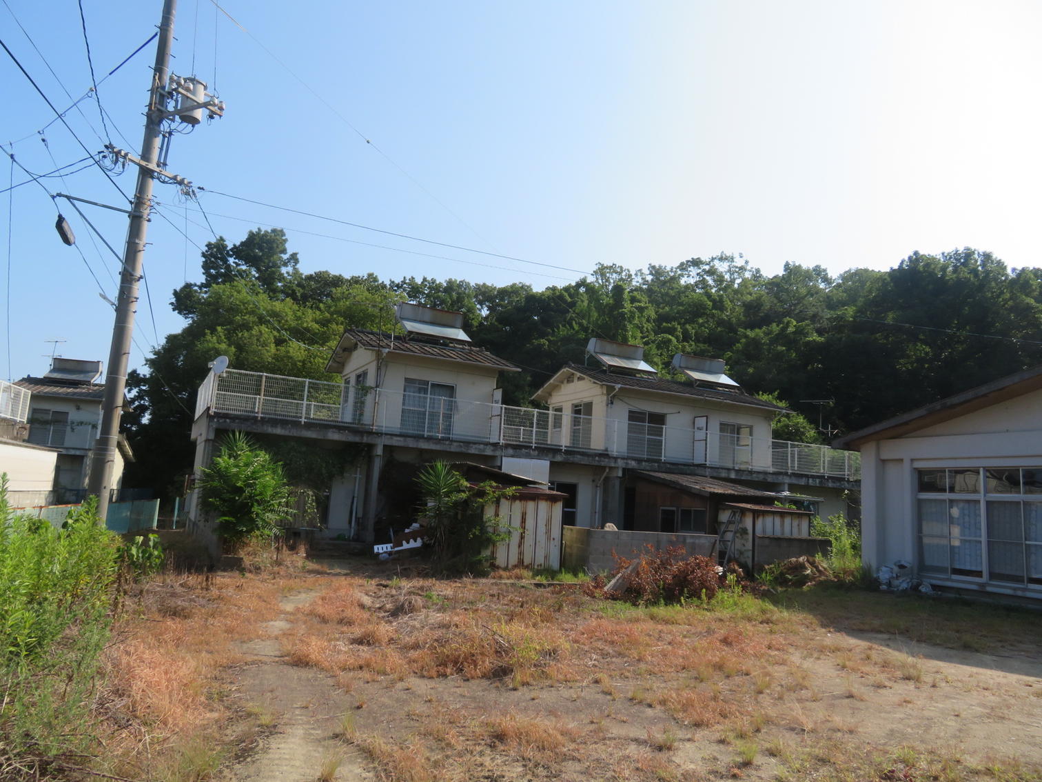 屋上に手すりを回した2階建てが同じ形で並ぶ。屋根に温水器やソーラーパネルが載る。