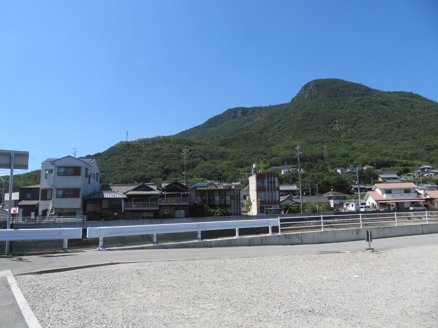 砂利の空き地の向こうに家並みと山が見える。